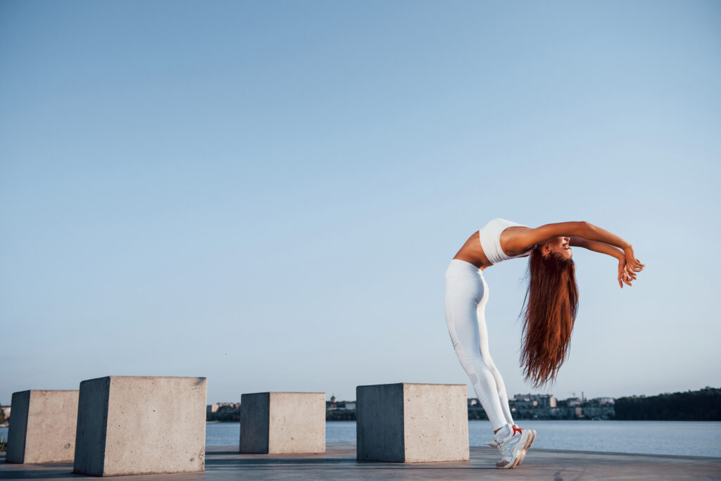 Shot of sportive woman doing fitness exercises near the lake at daytime